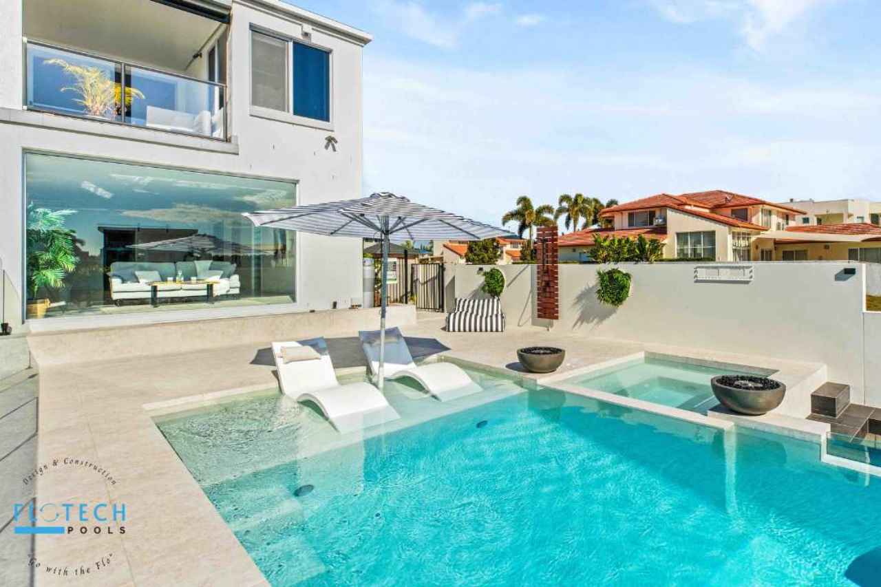 Modern custom concrete swimming pool with built-in loungers, umbrella shade, integrated spa, and tiled surrounds in a luxury Gold Coast backyard.