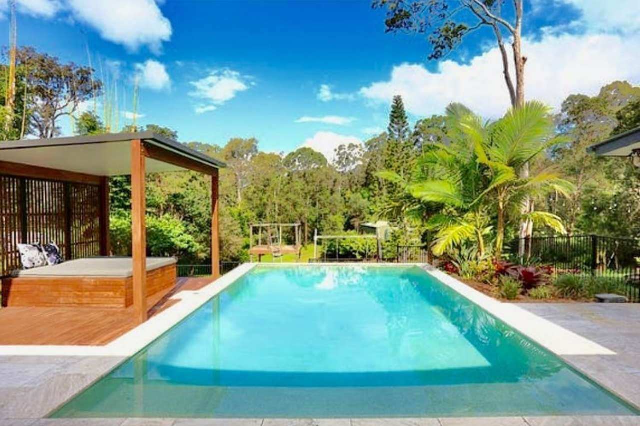 Rectangular concrete swimming pool with timber deck, shaded cabana, and tropical landscaping in a private Gold Coast backyard.