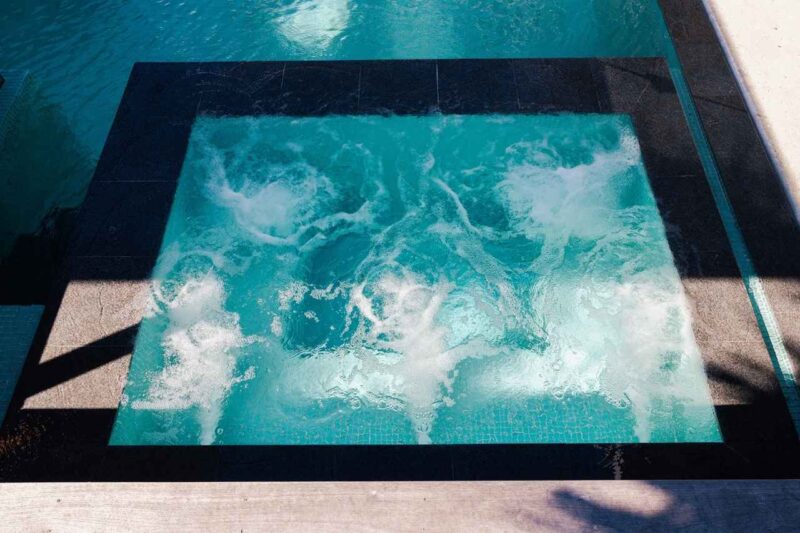 Luxury infinity-edge swimming pool with integrated bubbling spa section, showcasing modern concrete design and crystal-clear turquoise water.