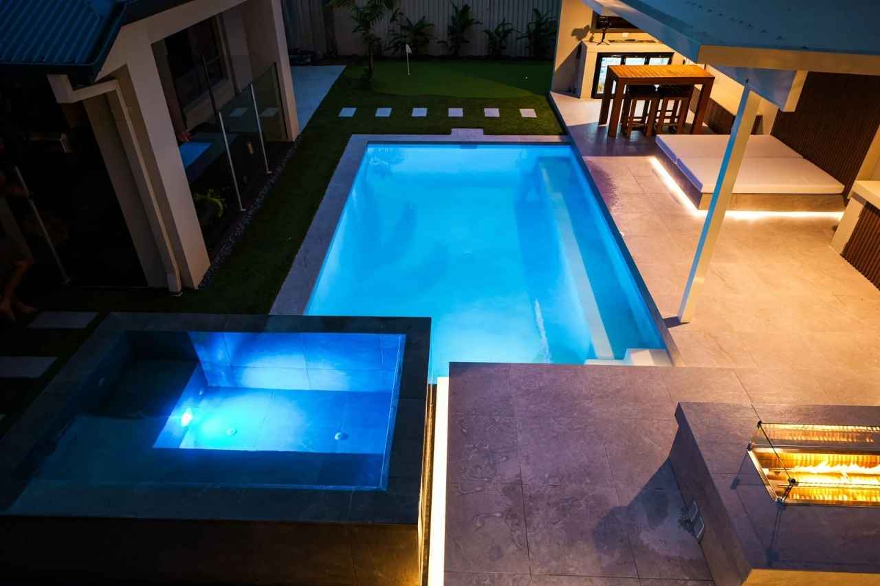 Luxury pool in Gold Coast with illuminated spa, modern patio, and outdoor entertaining area featuring lounge and dining space.