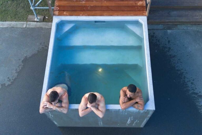 Three men relaxing in the Plungie Quad, a 2.2m x 2.2m square precast concrete plunge pool filled with water, next to a timber deck.