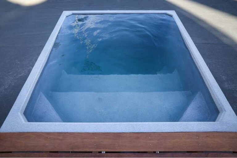 Front view of the Plungie Quad, a 2.2m x 2.2m square precast concrete plunge pool with built-in steps, filled with clear water and positioned next to a timber deck.
