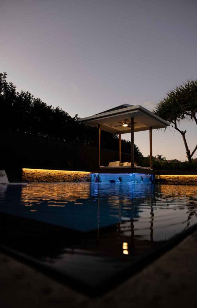 Modern concrete swimming pool on the Gold Coast with feature lighting, cabana, and luxury outdoor design at dusk.