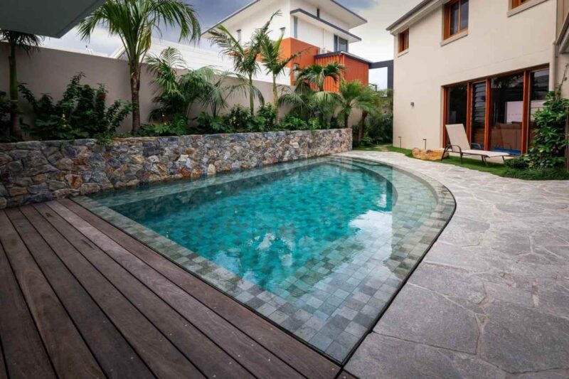 Family-friendly rectangular concrete swimming pool with wide entry steps, modern white deck, sun loungers, and an outdoor entertaining pavilion in a Gold Coast backyard.