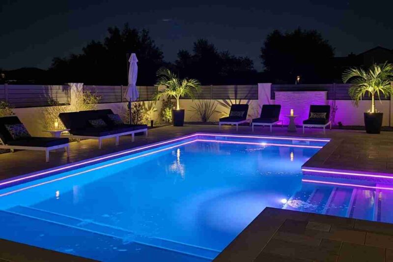Night shot of a renovated backyard pool glowing with blue and purple LED lighting, creating a luxury resort-style effect.