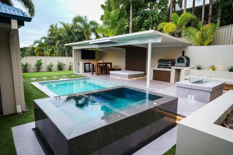 Modern residential backyard after pool renovation featuring a luxury concrete swimming pool with spa, tiled surrounds, outdoor kitchen, and entertaining area in a Gold Coast home.