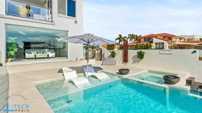 custom-concrete-pools (1) Modern custom concrete swimming pool with built-in loungers, umbrella shade, integrated spa, and tiled surrounds in a luxury Gold Coast backyard.